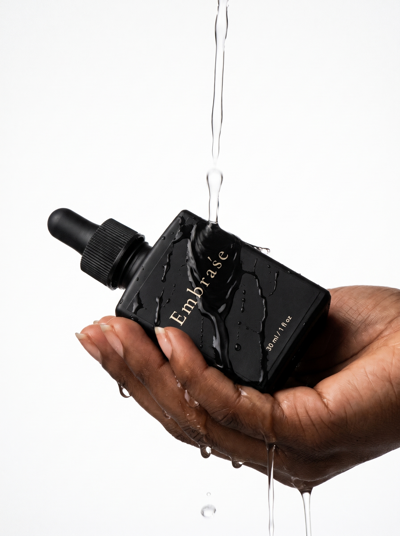 Hands holding the Embraśe Bakuchiol Anti-Aging Serum bottle under running water